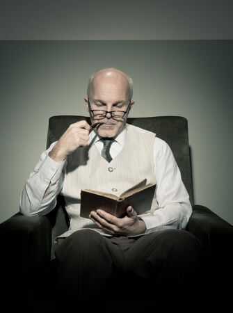Senior handsome man reading in armchair and smoking pipe.の写真素材
