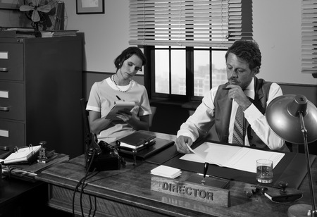 Director and secretary working together at desk, 1950s style office.の写真素材