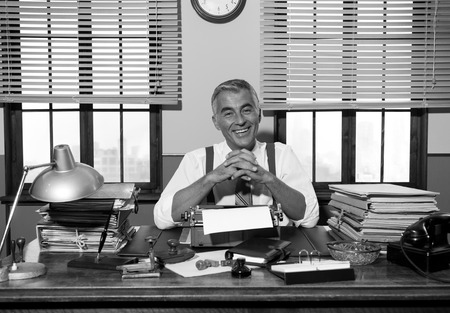 Smiling reporter working at office desk with vintage typewriter, 1950s style.の写真素材
