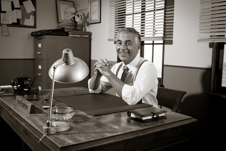 Cheerful director sitting at office desk, 1950s vintage office.の写真素材