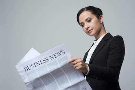 Attractive confident businesswoman with black jacket holding financial newspaper.の写真素材