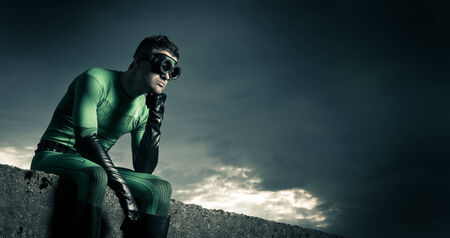Pensive superhero with hand on chin and dramatic cloudy sky on background.の写真素材