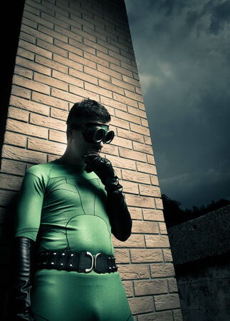 Cool superhero with hand on chin leaning to a brick wall.の写真素材