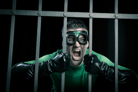 Angry green superhero shouting behind steel prison bars.の写真素材