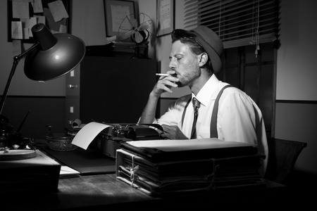 Retro reporter working late typing on a typewriter and smoking a cigarette.の写真素材