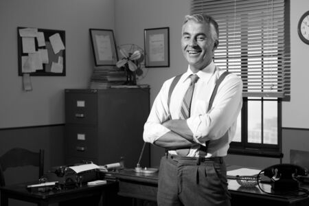Confident smiling businessman with arms crossed, 1950s style office.の写真素材