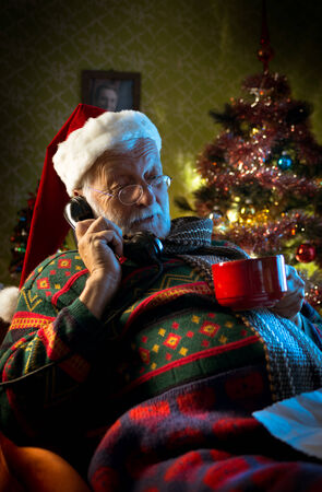 Santa Claus on the phone relaxing at home and holding a cup of tea.の写真素材