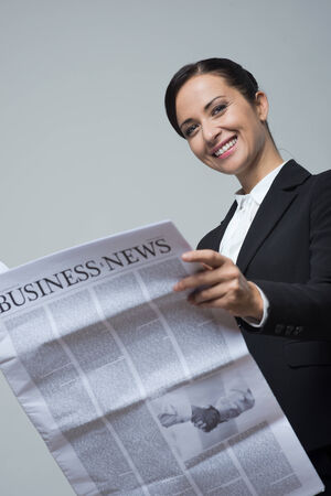 Attractive confident businesswoman with black jacket holding financial newspaper.の写真素材