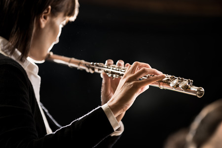 Elegant female flutist playing flute on dark background.の写真素材
