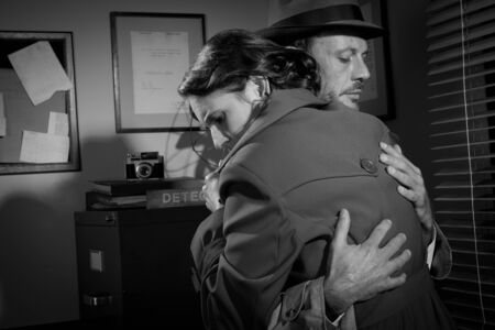 Detective consoling and hugging a young woman in his office, film noir scene.