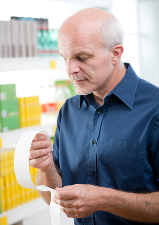 Attractive senior man checking a long receipt with store shelves on background.の写真素材
