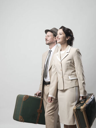 Elegant vintage couple walking and holding suitcases, travel concept