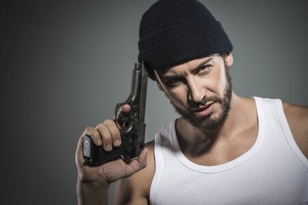 Handsome aggressive criminal with cap holding a gunの写真素材
