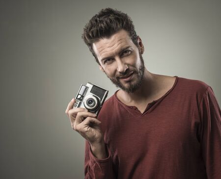 Young confident man holding a vintage camera and smilingの写真素材