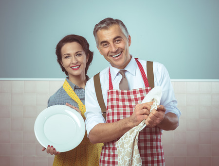 Smiling vintage couple in apron dish washing togetherの写真素材