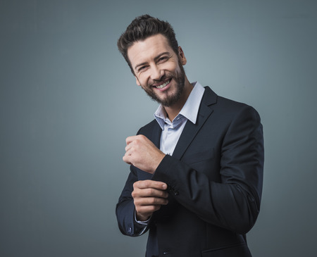Elegant young man adjusting his jacket and looking at cameraの写真素材