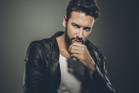 Cool seductive man in black leather jacket flirting and looking at cameraの写真素材