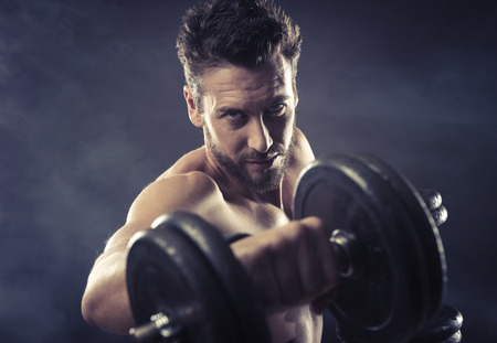 Attractive shirtless man exercising and lifting weights on dark background, strength conceptの写真素材