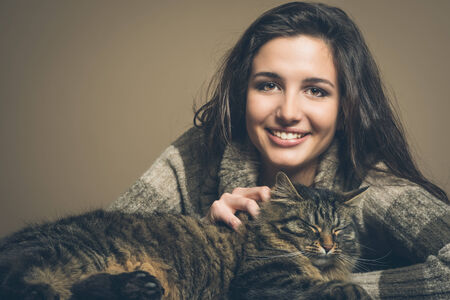 Beautiful woman cuddling a cat and smiling at cameraの写真素材