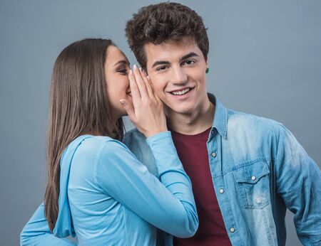 Young cute woman whispering secrets in her boyfriend's ear