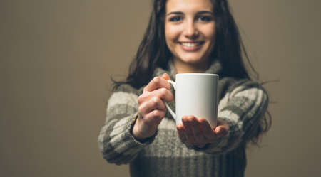Beatiful smiling young woman having an hot drink in a cupの写真素材