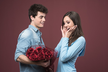 Smiling young woman receiving red roses as love gift from her boyfriendの写真素材
