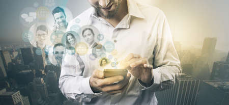 Businessman using a mobile touch screen phone with pictures of a group of people,  cityscape on...