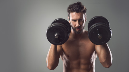 Confident attractive young man working out and weightlifting with dumbbells