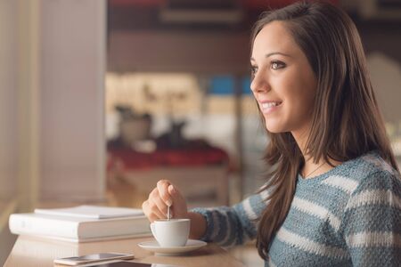 Smiling young woman at the cafe having an hot coffee cupの写真素材