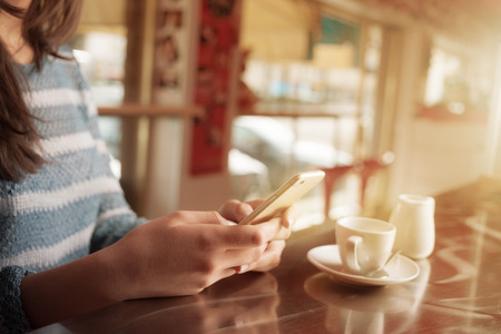 Woman leaning on the bar counter and text messaging with her mobile hands close upの写真素材