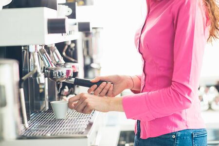 Young waitress making coffee with an espresso coffee machine she is holding a cup and the filter holderの写真素材