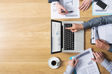 Business team hands at work with financial reports and a laptop blank copyspace on left top view
