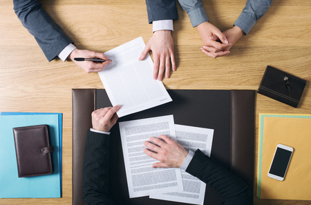 Business man and woman sitting at the lawyers's desk and signing important documents hands top view...
