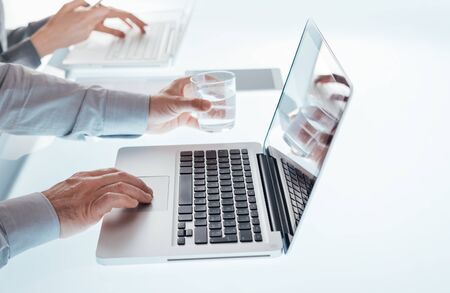 Business team working at office desk and typing on a laptop, hands close up, unrecognizable people