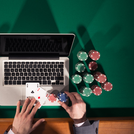 Man playing online poker with laptop on a green table with chips all around, top viewの写真素材