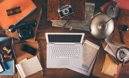 Messy vintage desktop with laptop, phone, lamp, camera and folders, top viewの写真素材