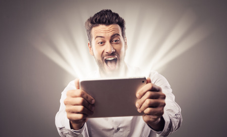 Cheerful smiling man watching videos and playing video games on his tablet