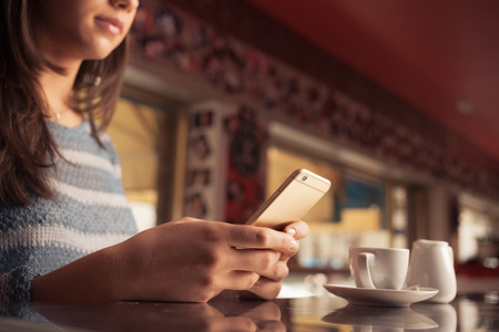 Woman leaning on the bar counter and text messaging with her mobile, hands close upの写真素材