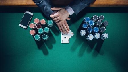 Elegant male poker player with smartphone holding two aces with stacks of chips all around, hands detail top viewの写真素材