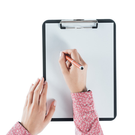 Young woman writing on a clipboard on a blank sheet against white background, hands close upの写真素材