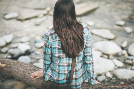 Young woman sitting along the river, relaxing and looking awayの写真素材