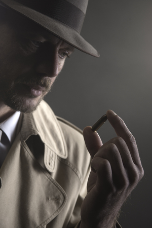 Handsome pensive detective holding a bullet, film noirの写真素材