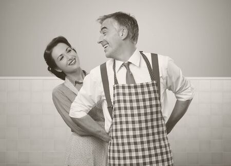 Vintage loving couple in the kitchen she is tying her husband's apron