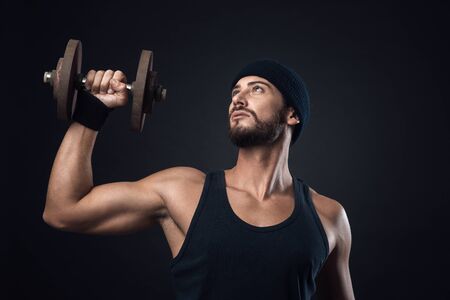 Cool confident man with cap lifting weights and working outの写真素材