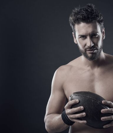 Handsome confident football player holding ball and showing his athletic bodyの写真素材