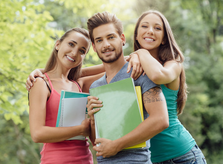 Back to school, group of young students and friends posing at the park, they are holding notebooks and smiling at cameraの写真素材