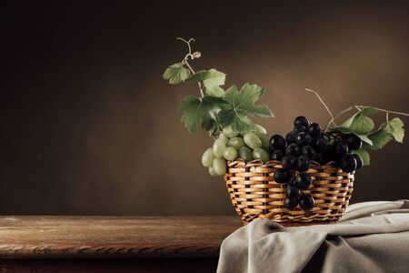Seasonal ripe grapes in a basket on a rustic wooden table, vine leaves and drape, classic still lifeの写真素材