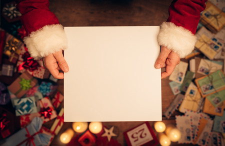Santa Claus holding a blank sign, hands close up, top view, desktop with Christmas gifts and letters on backgroundの写真素材