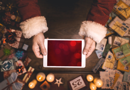 Santa Claus using a digital touch screen tablet, hands close up, top view, desktop with letters and Christmas gifts on backgroundの写真素材