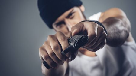 Handsome aggressive criminal with cap holding a gunの写真素材